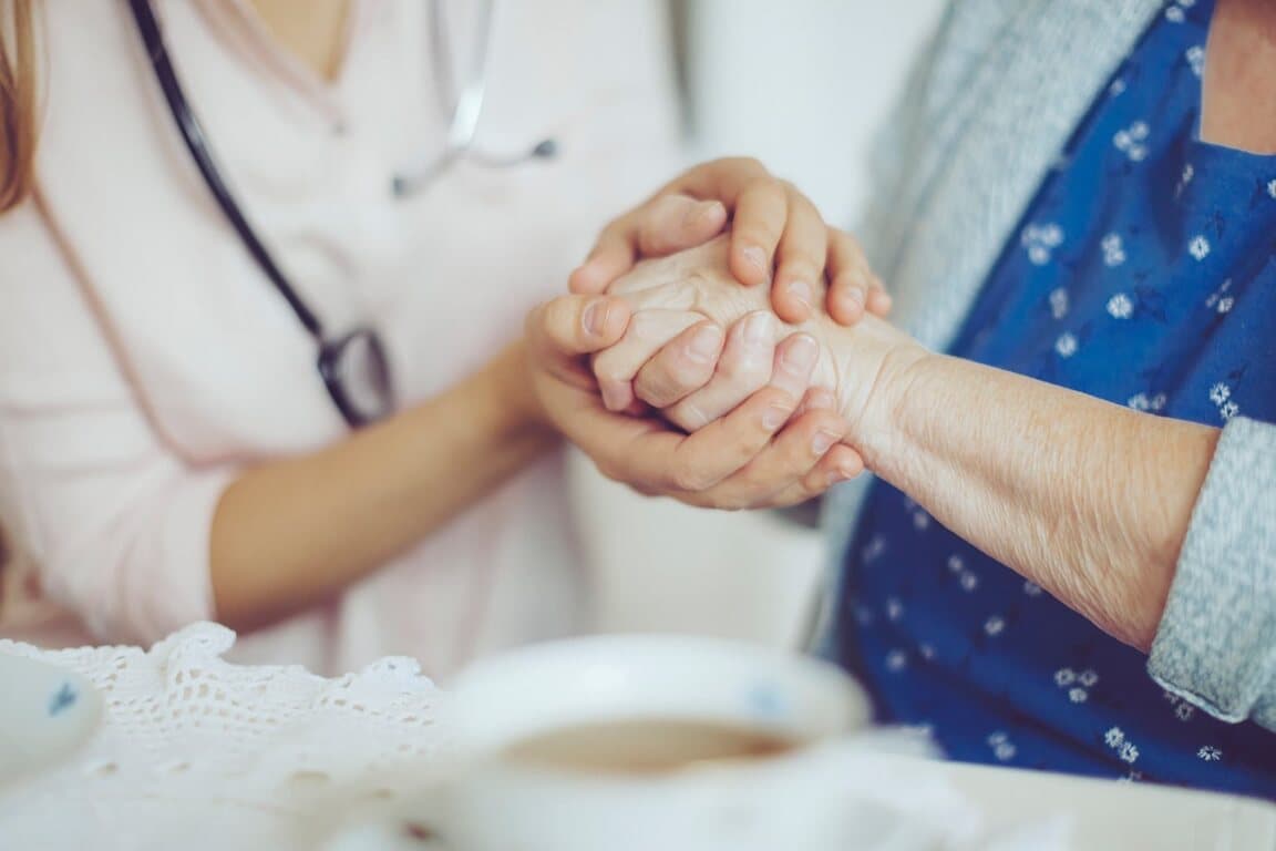 Geriatri doktoru gerontolog yaşlı kadının elini tutuyor.
