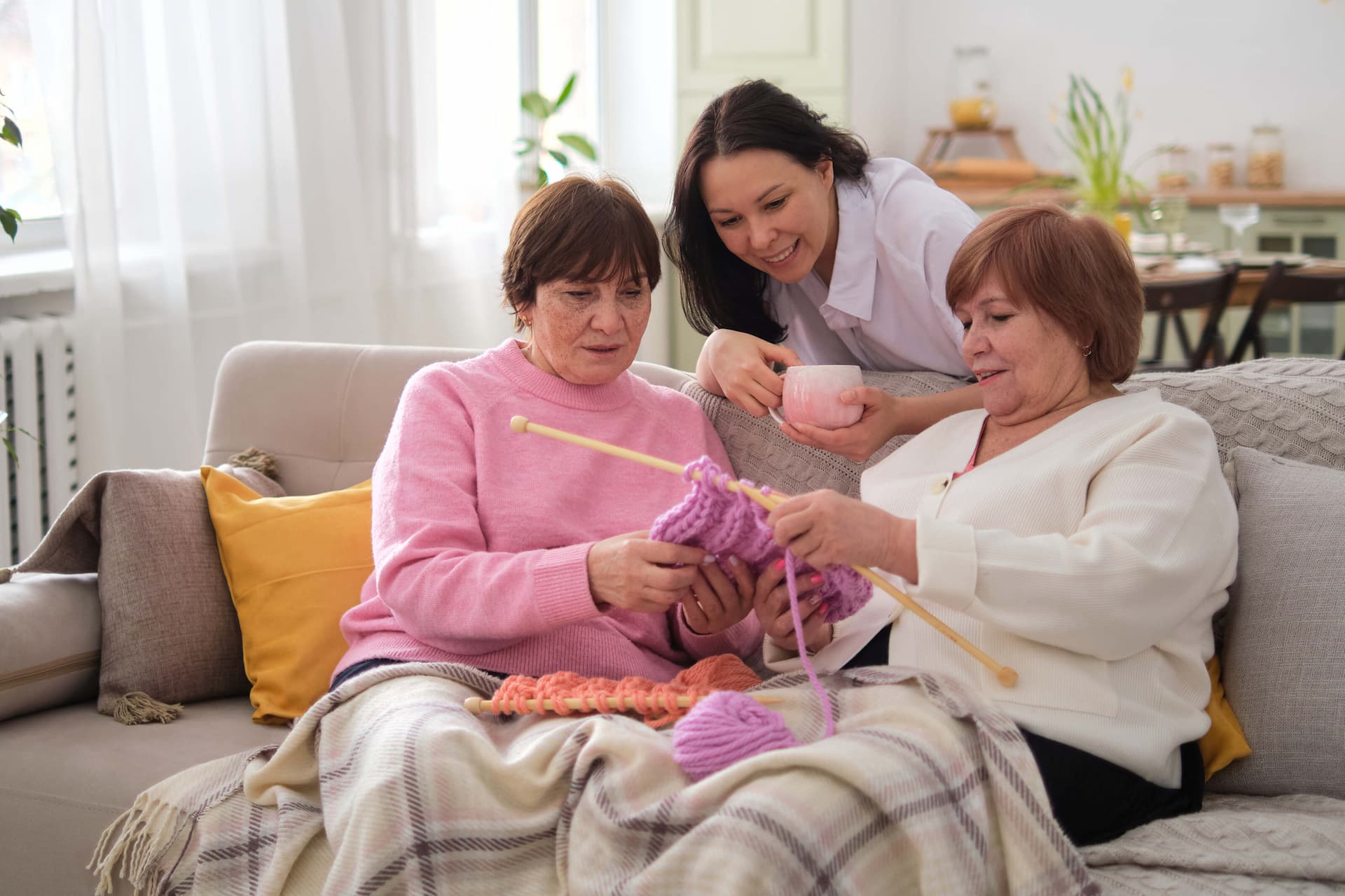 Yaşlı alzheimerlı kadınlar genç bakıcı ile örgü örmekte.