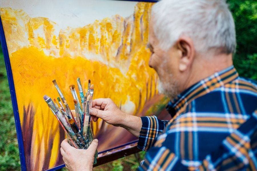 Yaşlı adam torunu ile birlikte açık havada tuvale resim yapıyor.