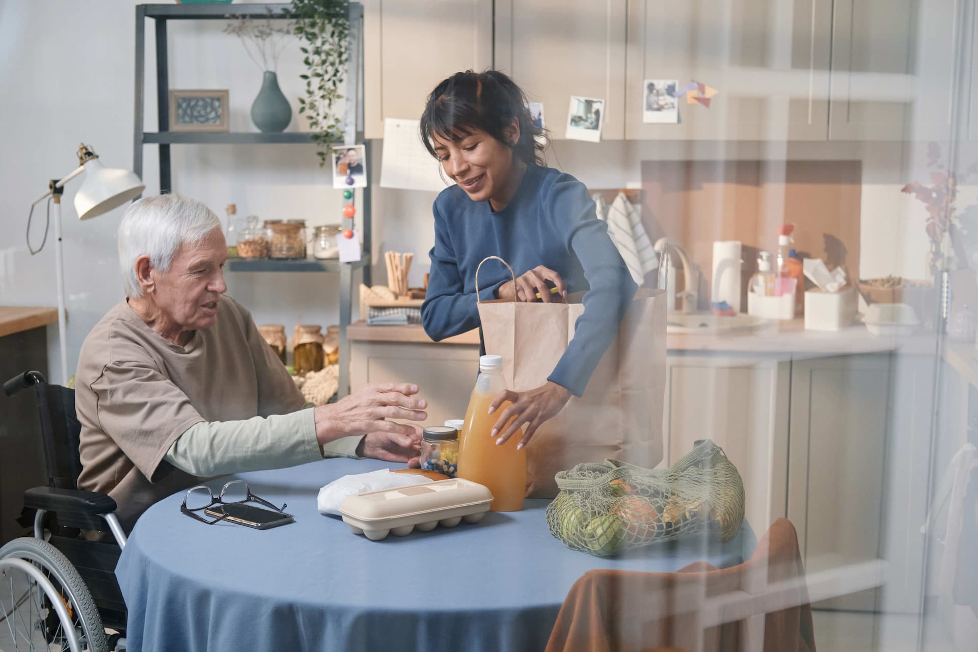 Bakım uzmanı engelli yaşlı adam ile mutfakta alışveriş yerleştirmekte.